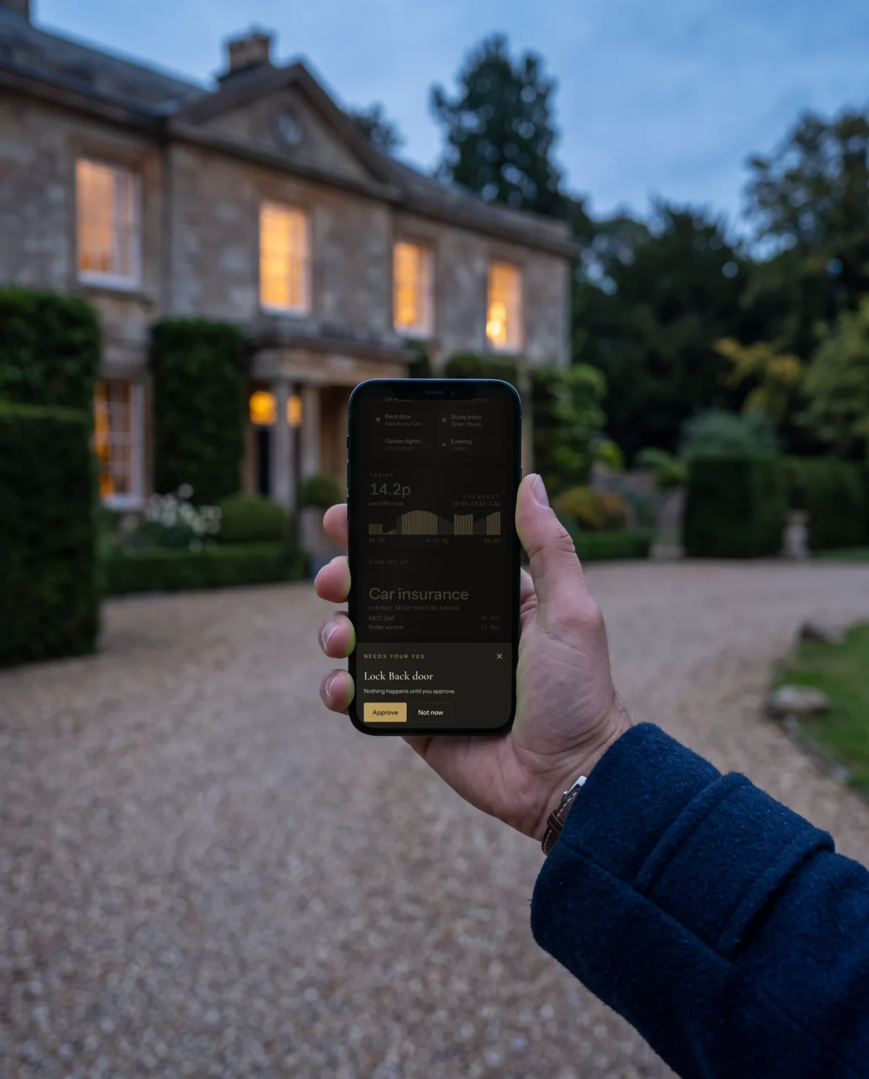 A hand holding a phone on a gravel drive at dusk, the house lit behind, the phone asking to lock the back door.